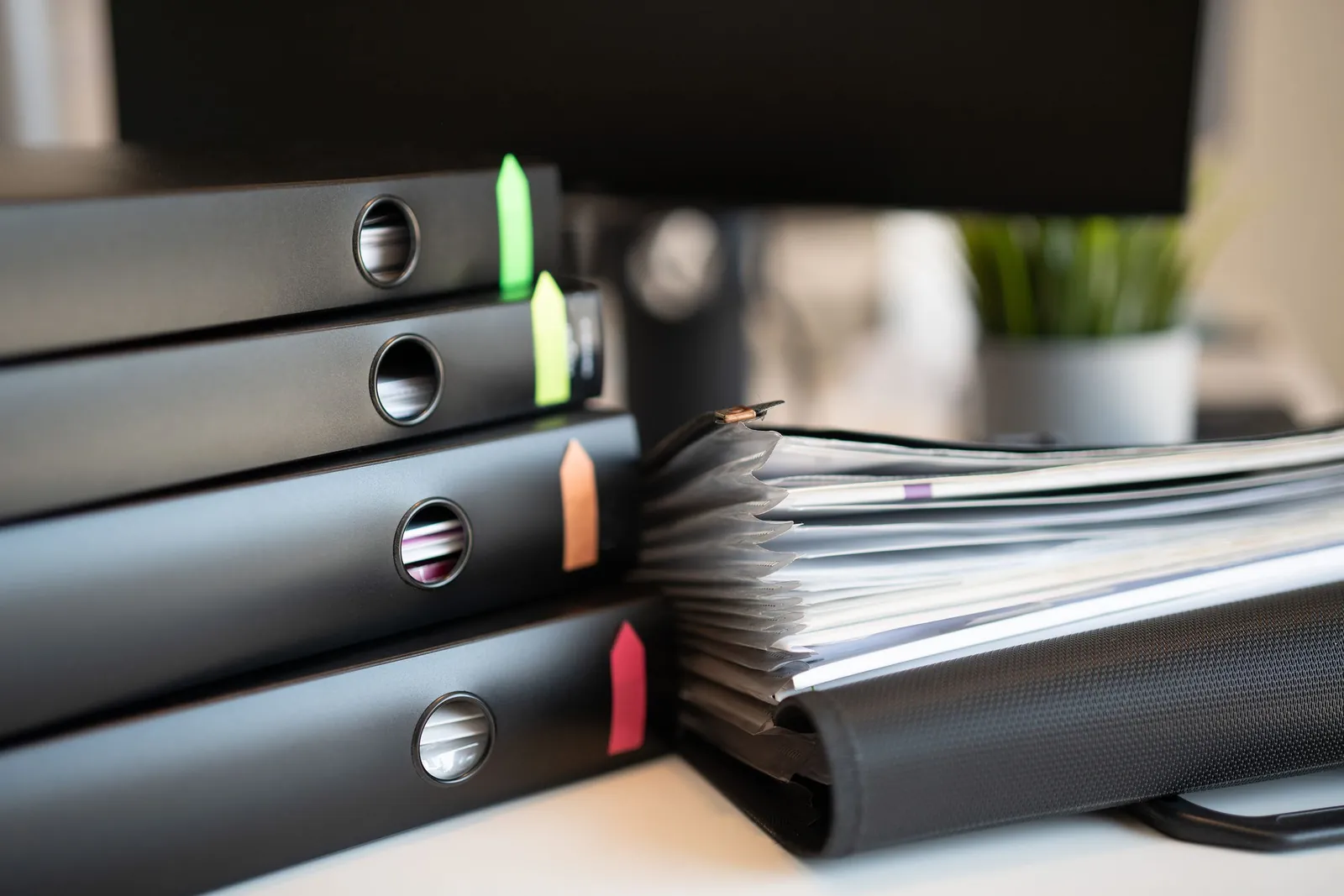 Stack of colorful ring binders holding filed invoices on an office desk