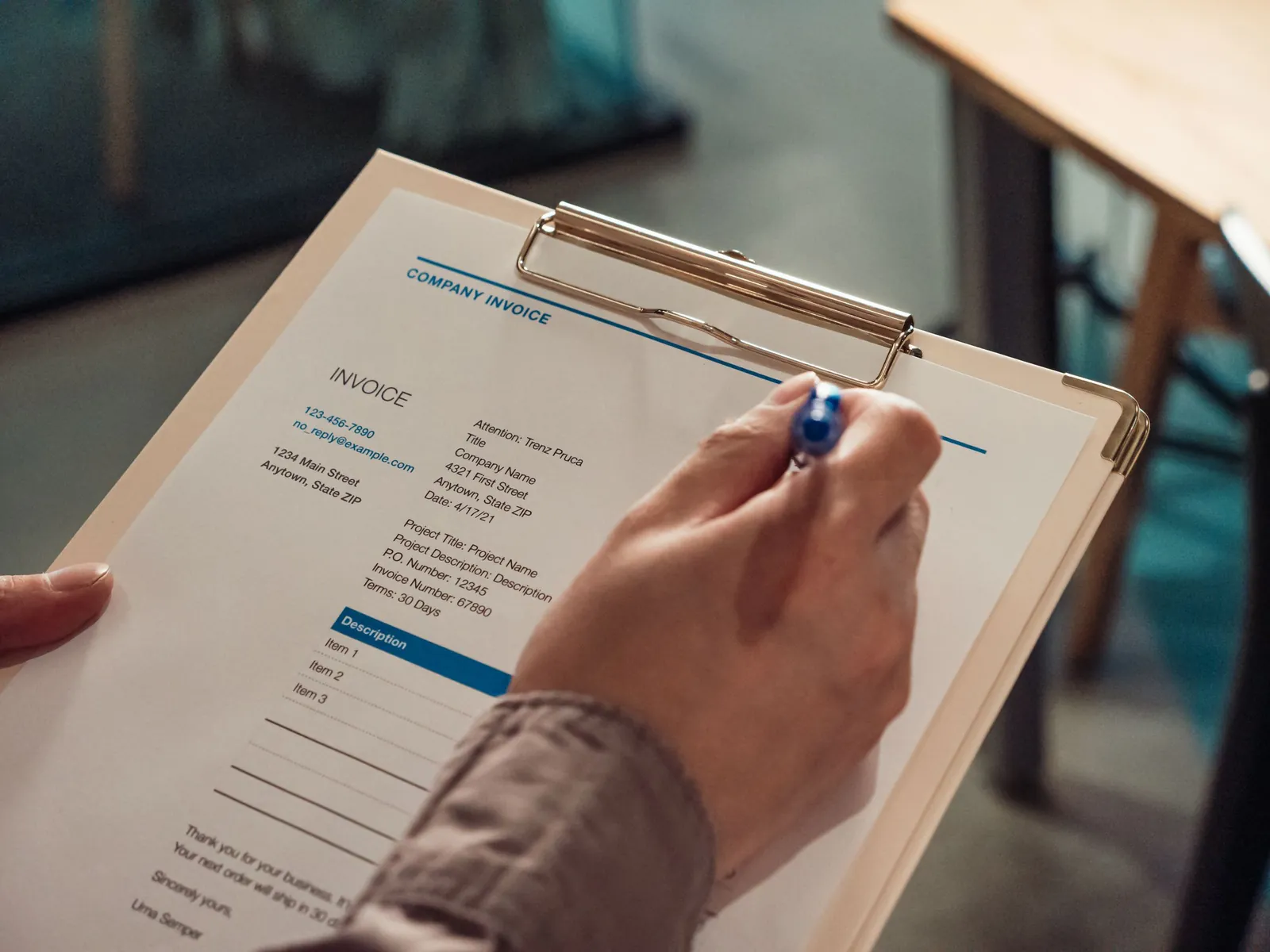 Person holding a printed company invoice on a clipboard with a pen